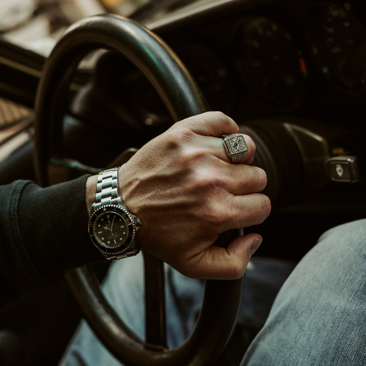 Man holding vintage steering wheel with watch and ring, classic motorsport interior detail
